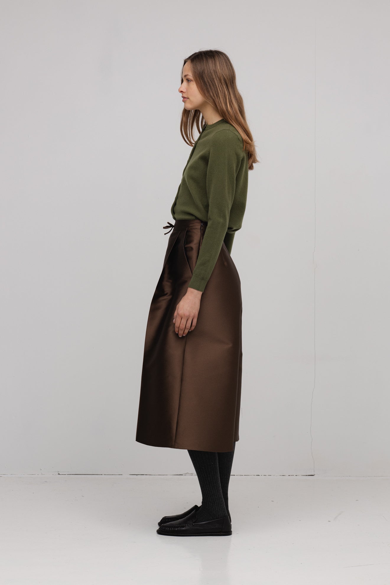 Woman wearing a green sweater and brown skirt on a white background