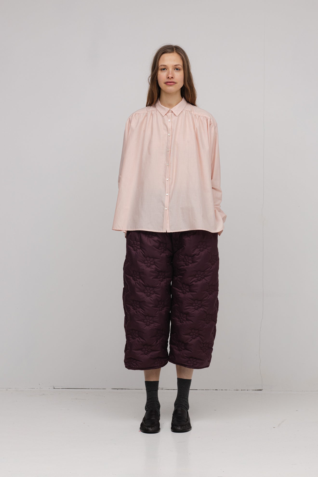 Person wearing a light pink blouse and dark purple pants on a white background