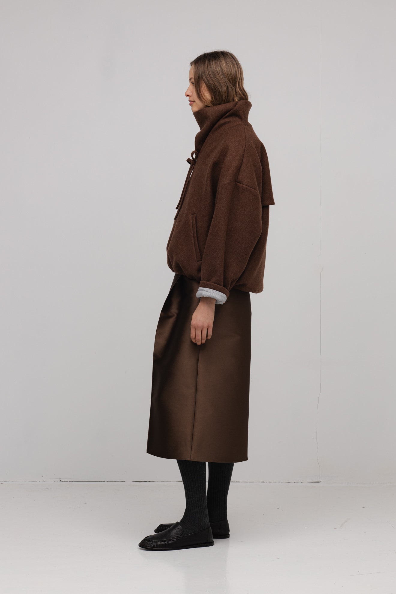 Person wearing a brown coat standing against a white background
