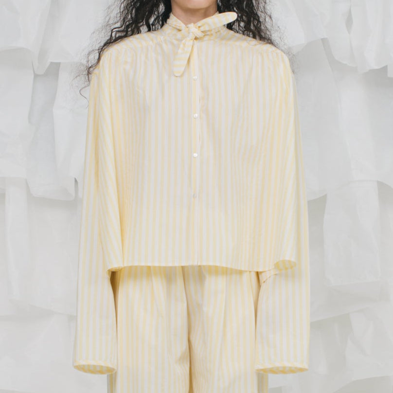 Person wearing a light yellow outfit against a textured white background