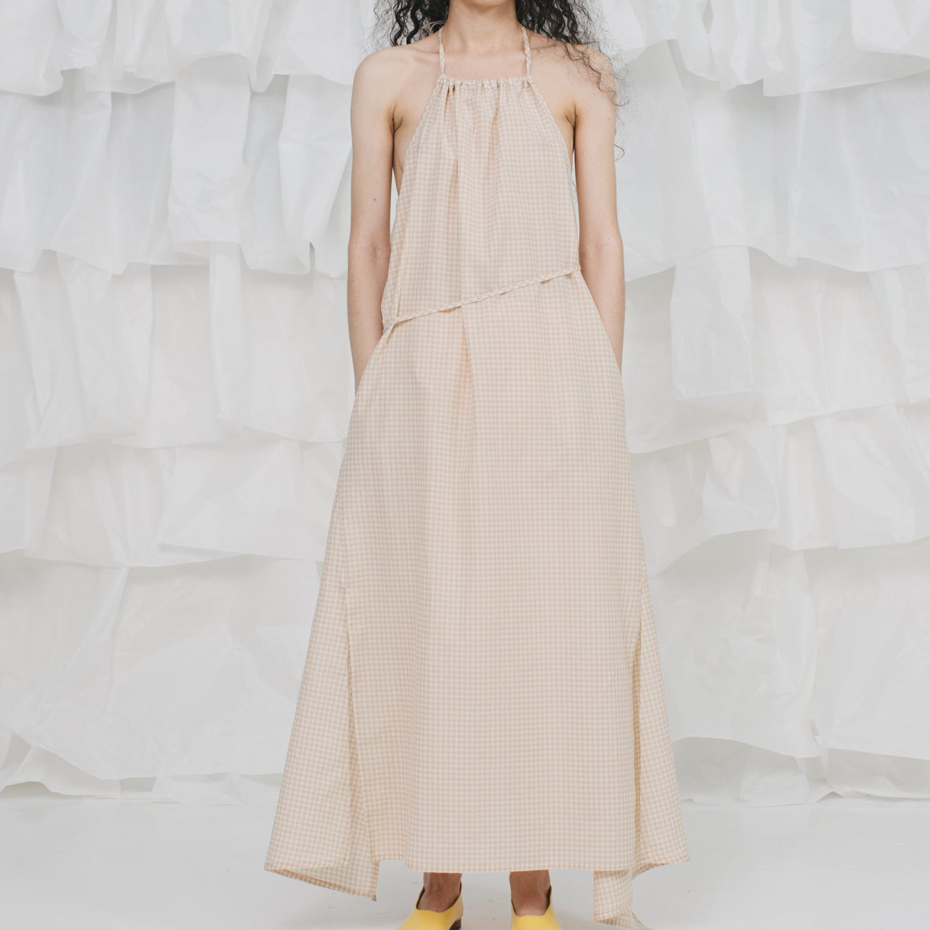 Woman wearing a beige dress standing against a textured white wall.