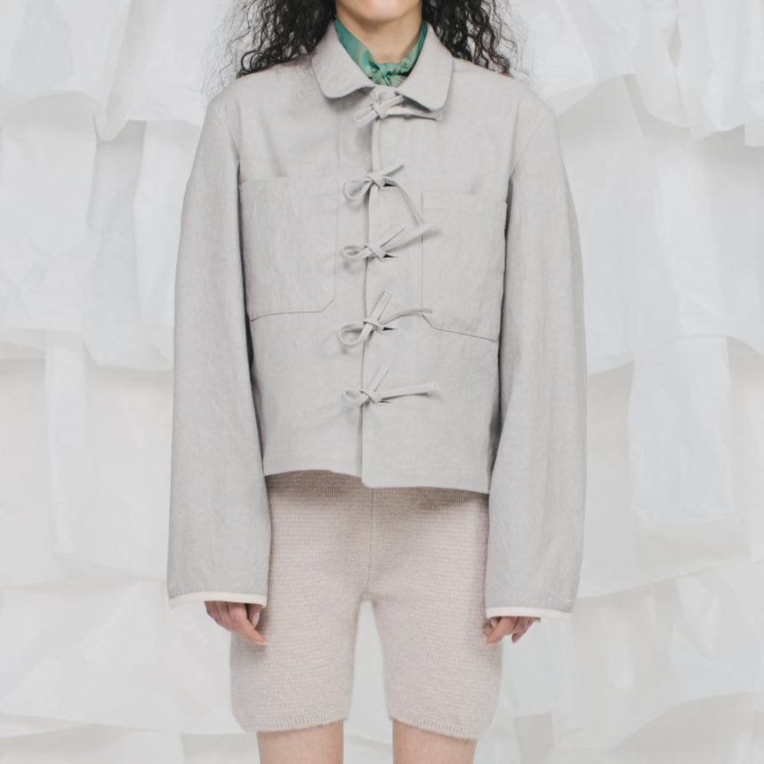 Person wearing a light gray jacket with button details on a white background