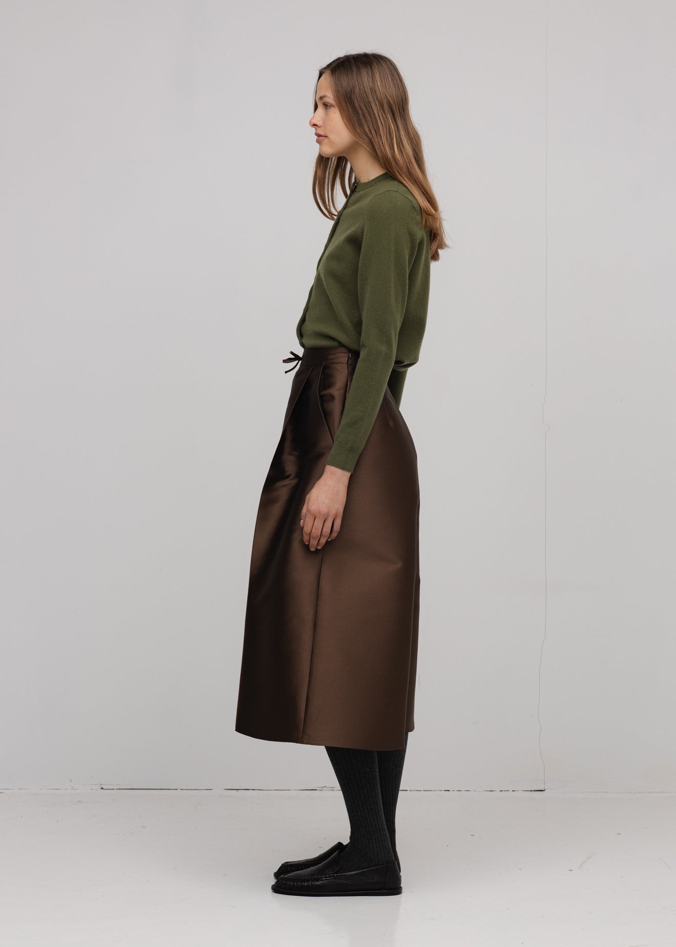 Woman wearing a green sweater and brown skirt on a white background