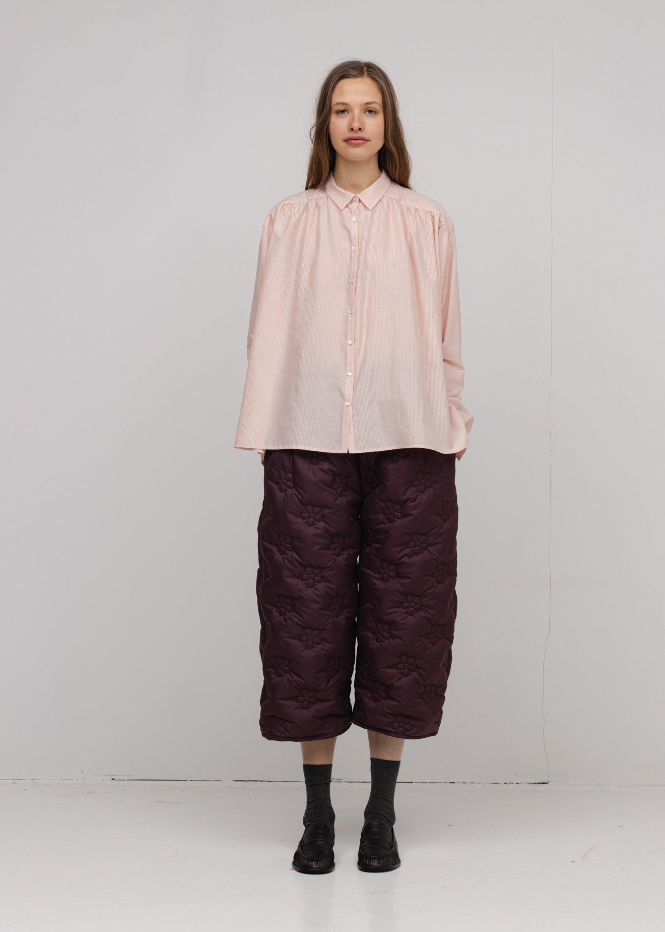 Person wearing a light pink blouse and dark purple pants on a white background