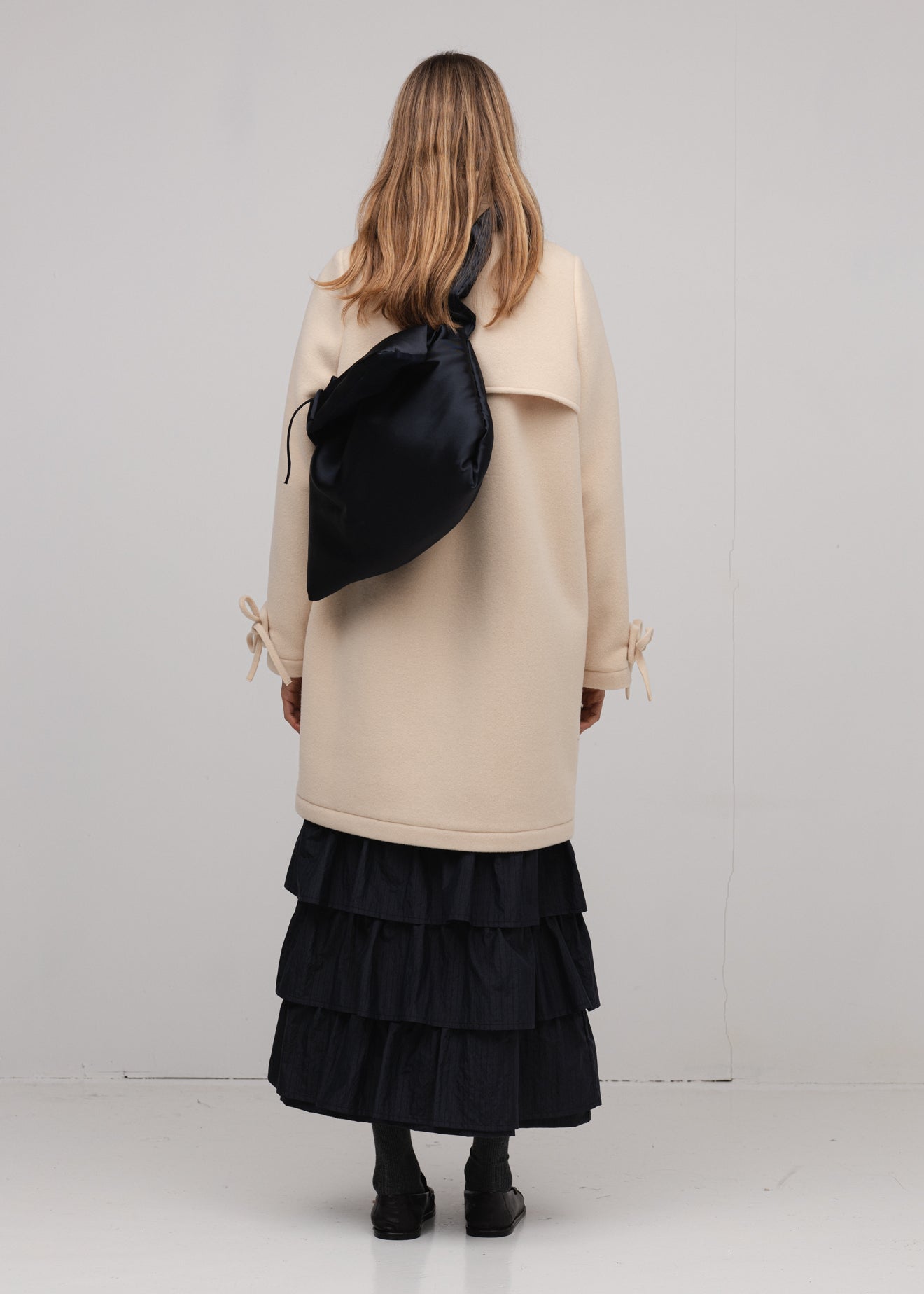Person wearing a beige coat and black ruffled skirt with a black bag on a white background